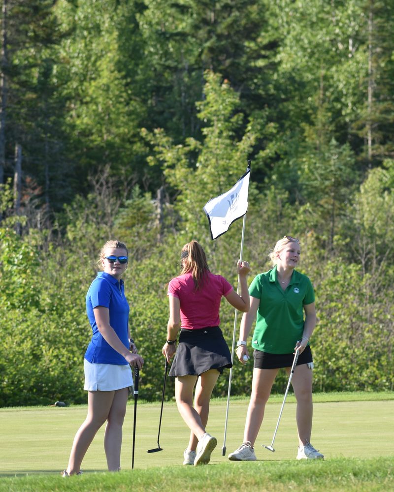 Three high school golfers walking off a New Hampshire green, one holding the pin.